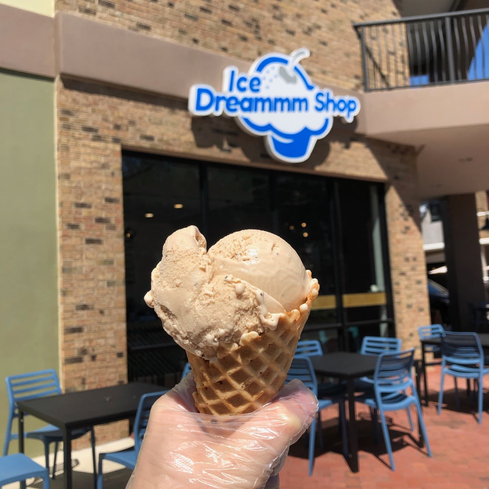 Scoop of homemade ice cream in a waffle cone held up outside the Ice Dreammm Shop Wesley Chapel storefront